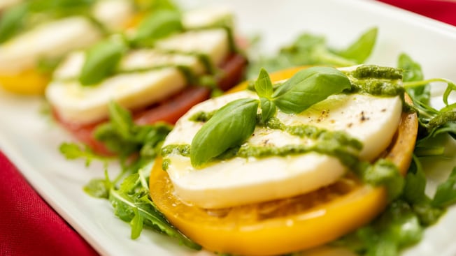 Mozzerella atop a tomato slice drizzled with a white balsamic pesto
