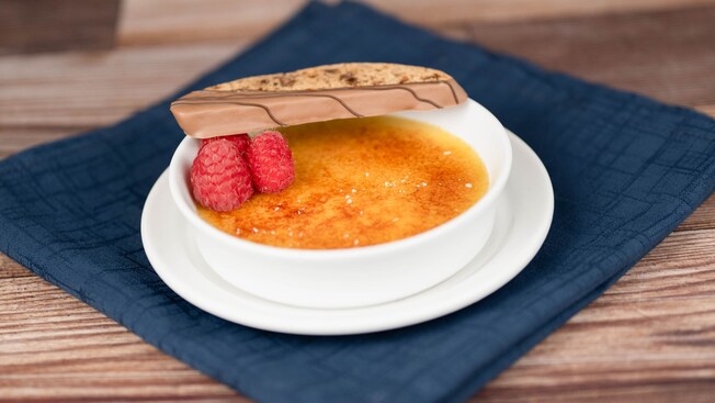 A bowl of Salted Caramel Creme Brulee with a caramel mocha biscotti and 3 raspberries