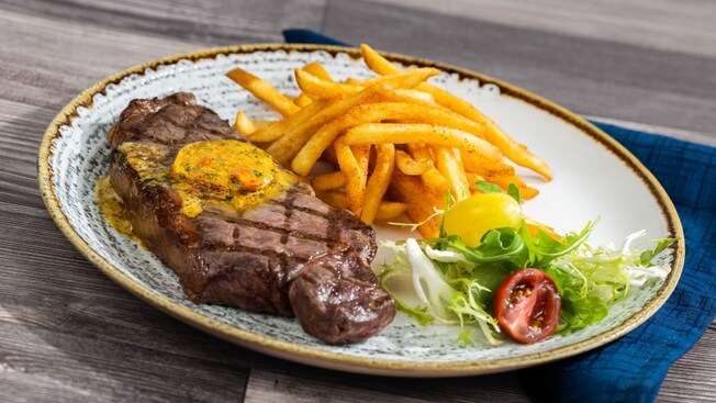 A plated meal with a grilled steak topped with butter, served with seasoned fries and a small salad