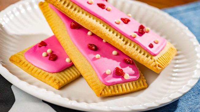 Pastries topped in frosting, bacon and candy resting on a plate and a tablecloth