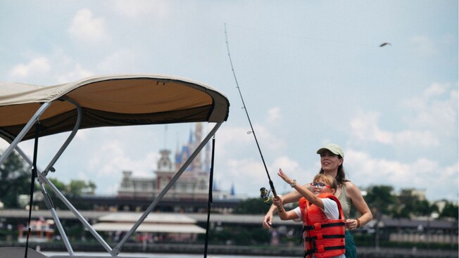 A mother observes as her daughter casts a line with a lure over the side of a boat