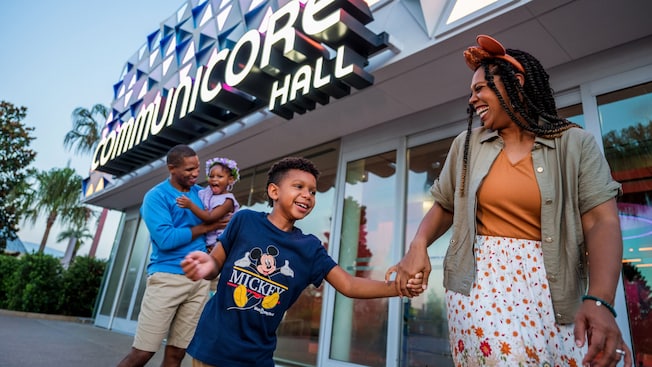 A smiling family of 4 walking by the main entrance to CommuniCore Hall at Epcot