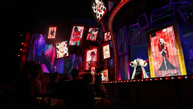 Cruella de Vil on stage with animated portraits of herself during Disney Villains, Unfairly Ever After at Disney’s Hollywood Studios