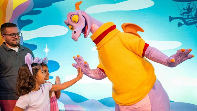 El dragón Figment choca palmas con 2 niños pequeños mientras su padre los mira y sonríe