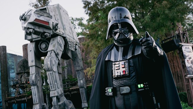 Darth Vader posing in front of an Imperial walker near the entrance to the Star Tours The Adventures Continue attraction in Disney’s Hollywood Studios