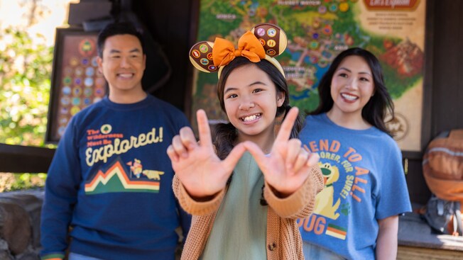 A young girl in a Minnie Mouse ear headband making the letter W with her hands while her parents look on
