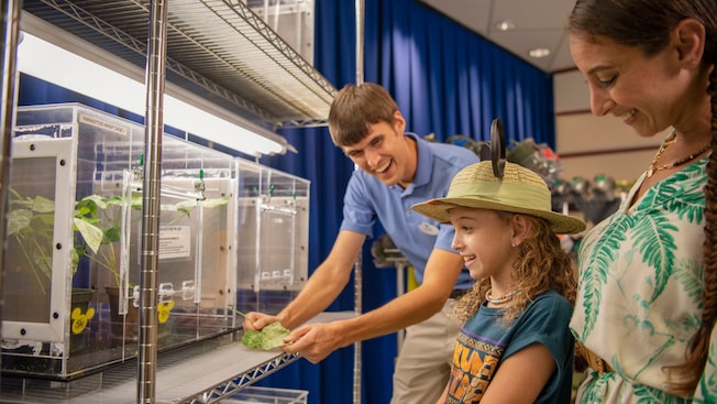 A Cast Member holds a leaf while showing a display to a mom and her daughter