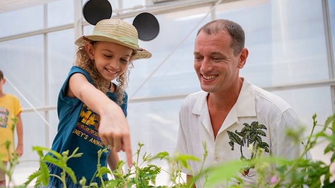 A little girl smiles with her dad and points at a plant