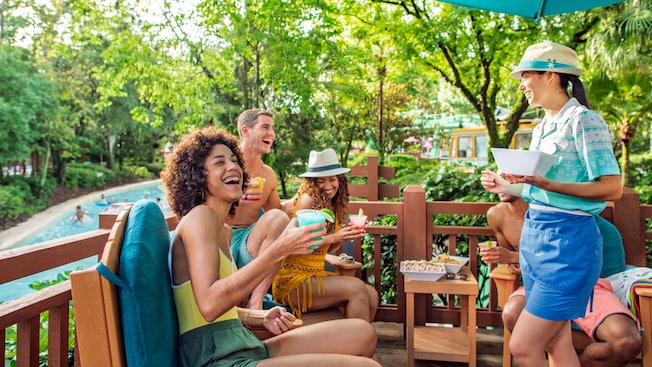 A Cast Member taking drink orders from 3 laughing Guests on a shaded deck at Disney’s Blizzard Beach water park