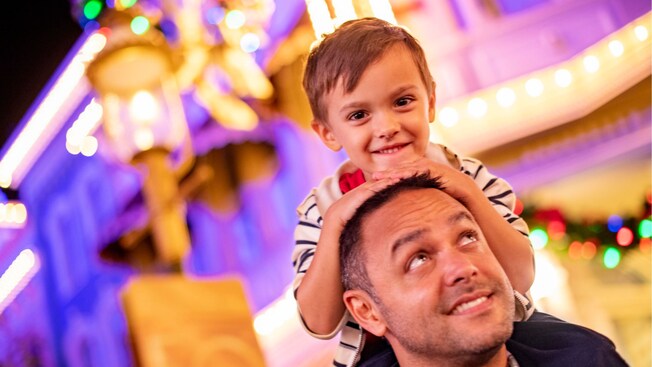 A child sitting on his father’s shoulders at Main Street U S A in Magic Kingdom park