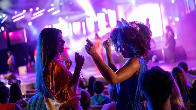 Two Guests dancing together in a concert venue with and a live music performance on a stage