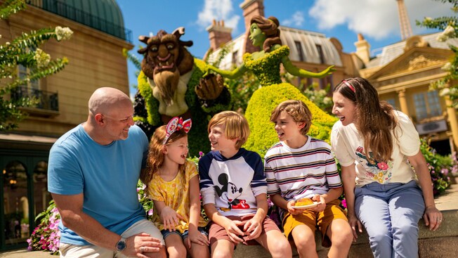 Family of 5 sitting together in front of a topiary of Belle and the Beast