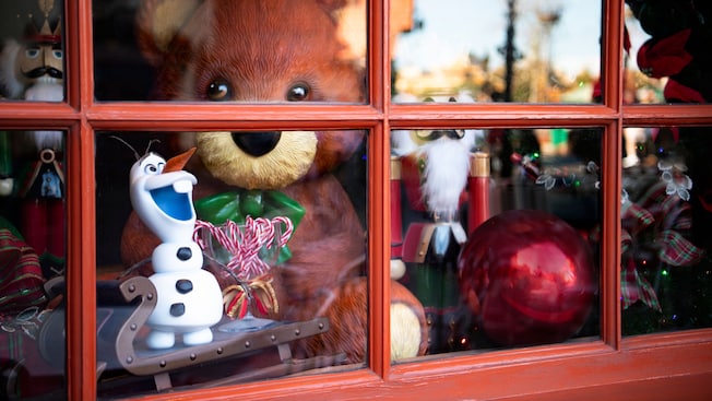 Un oso de peluche, un cascanueces y una figurita de Olaf en la ventana de una tienda