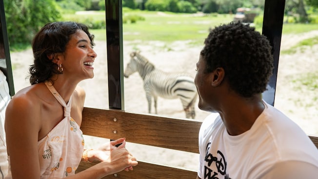 Un hombre y una mujer en un tranvía con una cebra en segundo plano en Harambe Wildlife Preserve