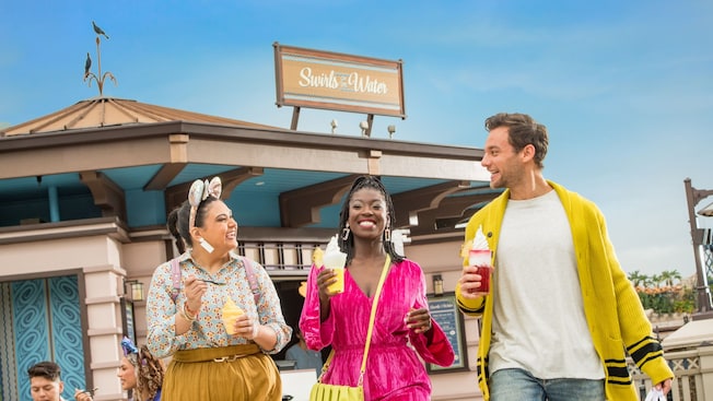 A group of 3 friends walking down Disney Springs while enjoying desserts from Swirls on the Water