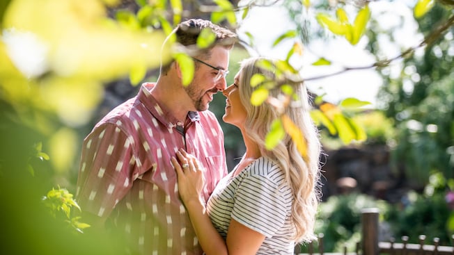 A man and a woman smile at each other near leafy trees