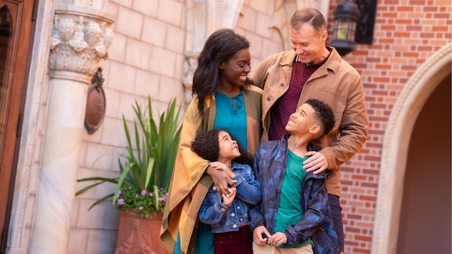 A family of 4 hug while standing near a brick building