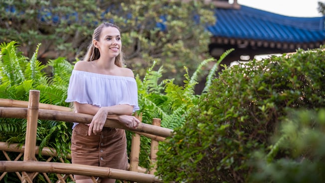 A woman stands on a bridge surrounded by bushes