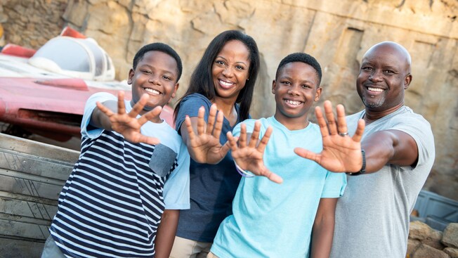 A family of 4, each person extending an arm as if to use the Force, near an A Wing Starfighter in Star Wars Galaxy's Edge