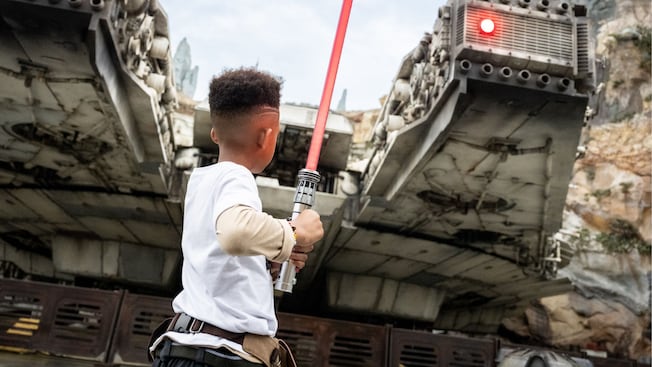 A young boy holding a lightsaber near the Millennium Falcon in Star Wars Galaxy's Edge