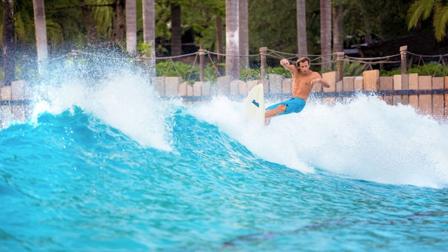 A man surfs a wave surrounded by palm trees