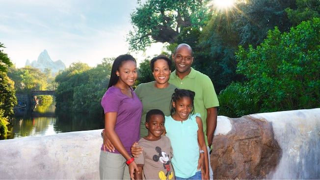 An African American father and mother pose with their three smiling children in Disney’s Animal Kingdom park, with the iconic Tree of Life in the background