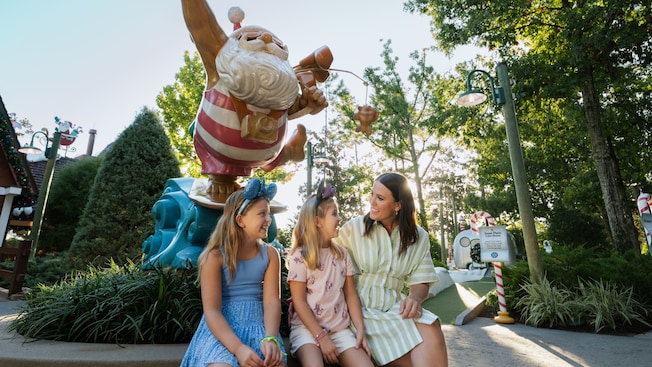 Two children sitting with their mother beneath a large statue of Santa Claus on a surfboard at Winter Summerland Miniature Golf