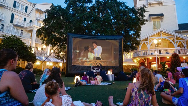 Familias en el césped miran The Princess and the Frog en un hotel en Walt Disney World por la noche