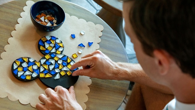 A man gluing stones onto a Mickey Mouse shaped object to create a mosaic art piece 