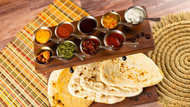An array of 10 sauces on a tray next to a plate of naan bread