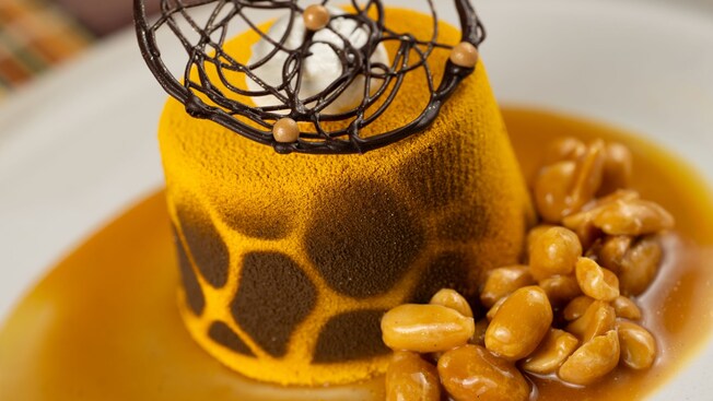Golden mousse cake topped with chocolate decoration next to a pile of peanuts