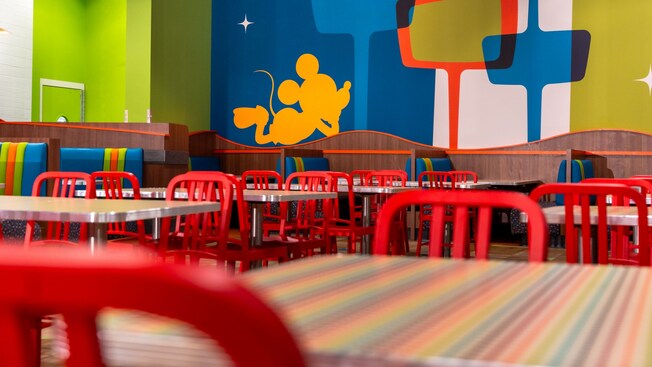 Dining tables and booths with a pop art mural featuring Mickey Mouse at Everything Pop Shopping & Dining in Disney’s Pop Century Resort