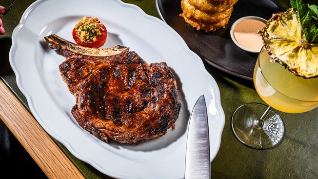 Un bistec Tomahawk, una torre de onion rings y un cóctel en Bourbon Steak