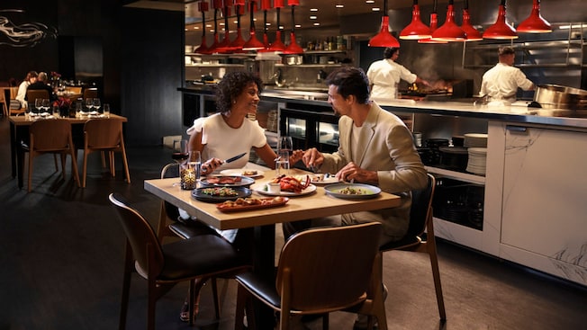 Una pareja riendo en una mesa junto a la cocina abierta de Capa