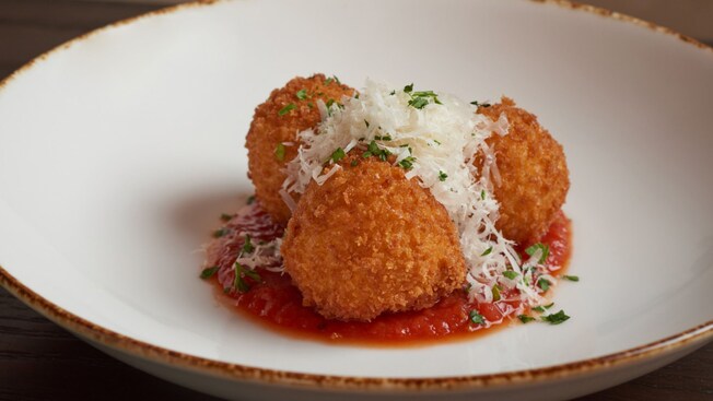 Three fried arancini over tomato sauce, topped with shaved cheese and herbs on a plate
