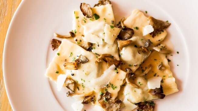 Ravioli with sautéed mushrooms, cream sauce and shaved cheese on a plate