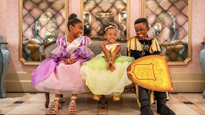 Two girls dressed as princesses and a boy dressed as a knight sitting on a sofa together