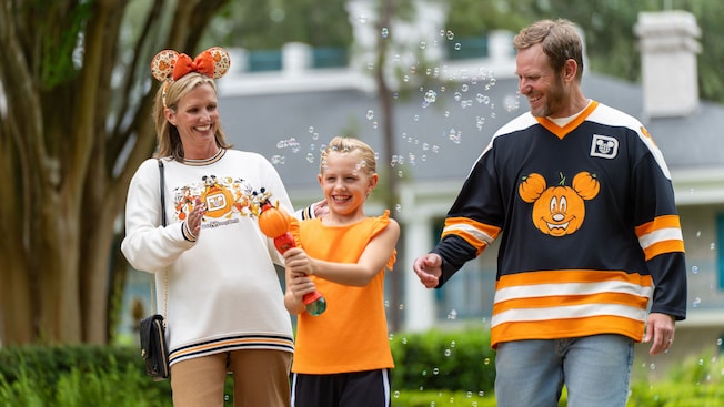 A family of 3 walking outdoors in Mickey's Not So Scary Halloween Party merchandise