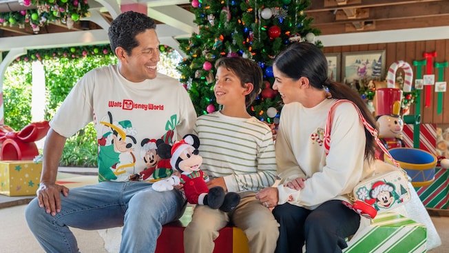 A family of 3 wearing Walt Disney World holiday merchandise