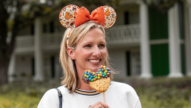 A Guest wearing a Halloween themed Minnie Mouse ear headband holds a Mickey Mouse shaped treat