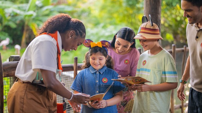 A family of 4 reading a Wilderness Explorer handbook along with a Cast Member in Disney's Animal Kingdom theme park