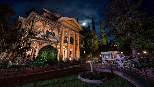 At nighttime, a horse drawn carriage sits outside the Haunted Mansion at Disneyland Park in California