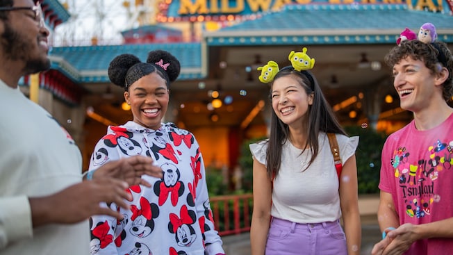 Cuatro Visitantes sonríen y hablan frente a Toy Story Midway Mania en Disney California Adventure Park