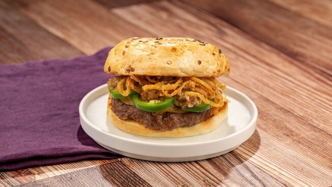 Una hamburguesa de carne de res con salsa de queso con jalapeño, cebollas crujientes y otros ingredientes en un panecillo de cebolla