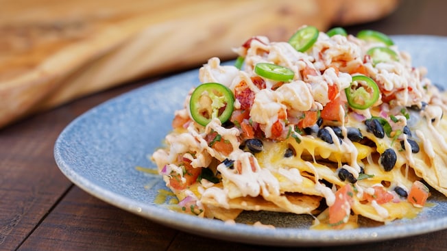 Plate of nachos topped with lobster, melted cheese, black beans, diced tomatoes, jalapeños and a drizzled sauce