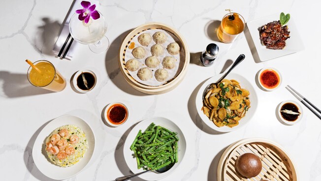 Table set with Asian inspired foods like dumplings, green beans and shrimp fried rice, with beverages, chopsticks and sauces