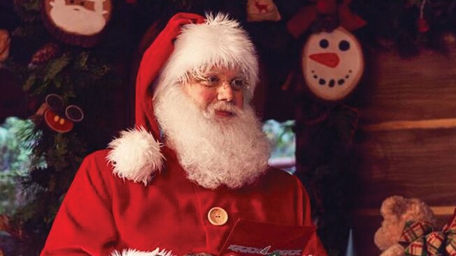 Santa Claus, smiling through his fluffy mustache and beard, holding a letter between his gloved hands