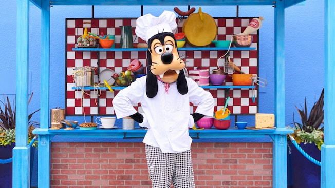 Goofy posing in a chef's outfit with a kiosk of cookware at Disney's California Adventure Park