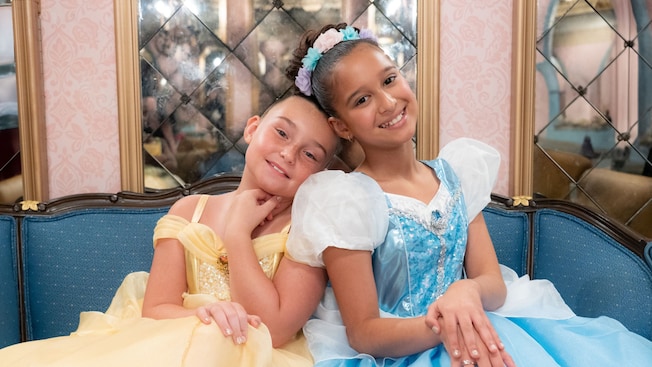Two girls in princess gowns sitting on a sofa in Bibbidi Bobbidi Boutique