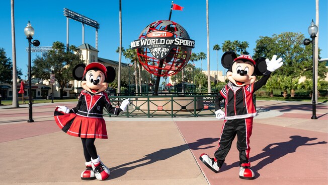 Minnie Mouse and Mickey Mouse standing near the ESPN Wide World of Sports Complex globe while dressed in sports themed attire